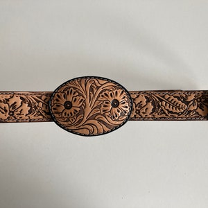 May include: A tan leather belt with a floral design and an oval buckle. The buckle is also decorated with a floral design.