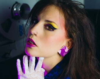 Könnte beinhalten: Eine Person mit auffälligem Make-up im 80er-Jahre-Stil, trägt eine blaue Jeansjacke und einen weißen Spitzenhandschuh. Sie hat ein Rosen-Tattoo und ist mit bunten Armbändern und geometrischen Ohrringen geschmückt. Der Hintergrund ist dunkel.