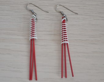May include: A pair of red and white dangle earrings with a silver hook. The earrings are made of thin, red cords with white wire wrapped around the top portion.