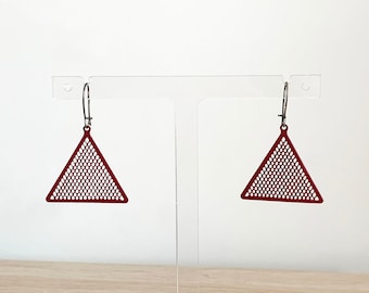 May include: A pair of red triangle earrings with a geometric pattern. The earrings are hanging from a clear acrylic stand.