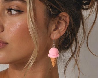 May include: A dangle earring featuring a miniature pink ice cream scoop atop a textured tan waffle cone. The charm is attached to a silver-toned metal hook wire, designed to hang from the earlobe with a simple and lightweight construction.