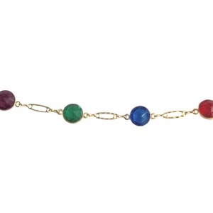 Puede incluir: Un delicado collar de oro con una serie de gemas facetadas y coloridas. Las gemas son en tonos de rojo, verde, azul y morado, conectadas por pequeños eslabones de oro. El collar se muestra sobre un fondo blanco.