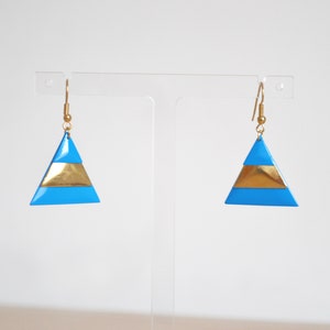 May include: A pair of gold and blue triangle earrings. The earrings are made of metal and have a geometric design.