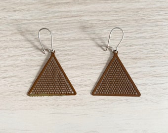 May include: A pair of geometric earrings. Each earring features a brown, triangle-shaped design with a mesh pattern. The earrings have silver-colored ear wires. The earrings are displayed on a light-colored wooden surface.