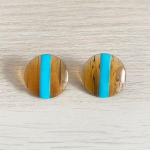 May include: A pair of round, brown and blue earrings. The earrings have a wood-like pattern and a blue stripe down the centre.