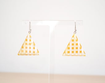 May include: A pair of triangle-shaped earrings. Each earring features a yellow and white checkered pattern. The earrings are suspended from silver-colored hooks, and are displayed against a white background.