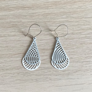 May include: A pair of pale grey teardrop earrings with a layered, openwork design. The earrings have a silver-coloured hook closure. The intricate pattern creates a delicate and modern aesthetic.