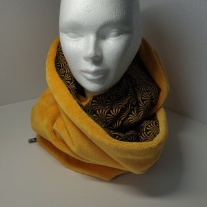 May include: Mustard yellow infinity scarf with a black and gold art deco pattern lining. The scarf is made of a soft, plush material and is draped around a white mannequin head.