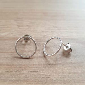 Peut inclure: Une paire de boucles d'oreilles créoles en argent avec un design circulaire simple. Les boucles d'oreilles sont petites et délicates, et seraient un excellent ajout à toute collection de bijoux.