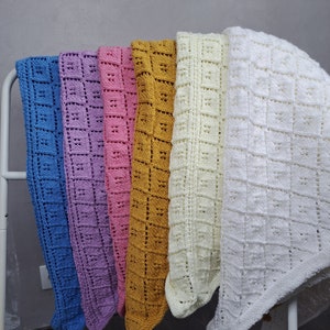 Peut inclure: Cinq couvertures pour bébé en crochet de différentes couleurs, dont bleu, violet, rose, jaune et blanc. Les couvertures sont accrochées à un support métallique blanc.