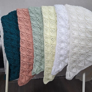 Könnte beinhalten: Sechs gehäkelte Babydecken in verschiedenen Farben, darunter türkis, rosa, grün, gelb und weiß. Die Decken hängen an einem weißen Metallgestell.