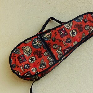 Könnte beinhalten: Eine rote und schwarze Gitarrentasche mit einem Vintage-Motorrad- und Totenkopfdesign.