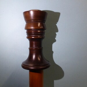 Puede incluir: Un remate de madera marrón oscuro con una parte superior redondeada y un diseño acanalado. El remate está unido a un poste de madera.