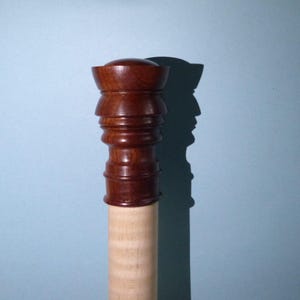 Può includere: Un bastone da passeggio in legno con una cima scolpita di colore marrone scuro e un fusto in legno di colore marrone chiaro.