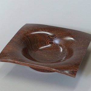 Op de afbeelding: Een donkerbruine houten kom met een vierkante vorm en een diep, afgerond interieur. De kom heeft een gladde, gepolijste afwerking en een natuurlijk houtnerfpatroon.