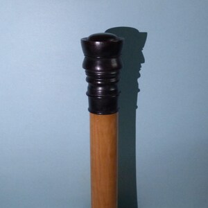 Puede incluir: Un bastón de madera con una parte superior negra tallada de forma intrincada.
