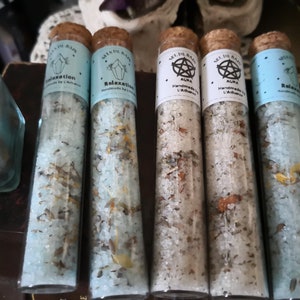 Puede incluir: Cinco tubos de vidrio llenos de sales de baño. Los tubos están etiquetados con el texto "Sel de Bain" y tienen diferentes diseños, que incluyen un cristal, un pentagrama y la palabra "Relaxation".