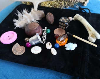 May include: A black velvet pouch filled with various small objects, including a pink button, a thimble, a seashell, a bone, a match, a dice, a feather, a small wooden object, a coin, and several beads.
