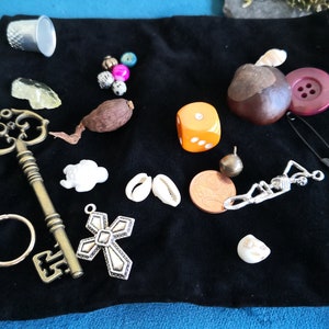 Peut inclure: Une collection de divers bibelots et breloques sur une pochette en velours noir. Les objets comprennent une clé, une croix, un dé, une coquille, un bouton, un dé à coudre, une pièce de monnaie, un charme squelette et quelques autres petits objets.
