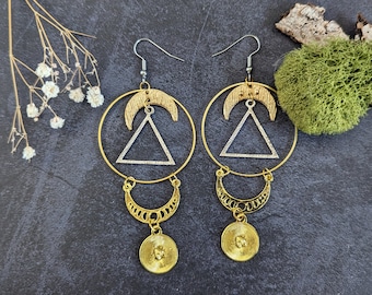 May include: Gold hoop earrings with a silver triangle pendant and a crescent moon charm. The earrings have a bohemian style.