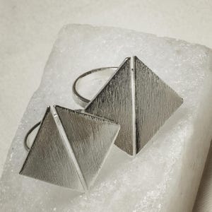 Peut inclure: Deux bagues en argent en forme de triangle avec une finition brossée. Les bagues sont empilées l'une sur l'autre.