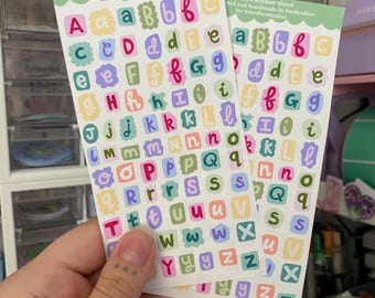 May include: Two sticker sheets featuring the alphabet in a variety of colours and fonts. The sheets are bordered in light green and have the text: "Letters sticker sheet Illustrated and handmade in Derbyshire by Arteafoxstudios."