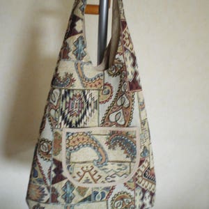 Könnte beinhalten: Eine beige und braune Tapisserie-Tragetasche mit Paisley- und geometrischem Muster. Die Tasche hat eine große Tasche auf der Vorderseite.