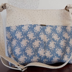 Könnte beinhalten: Eine weiße und blaue Blumentasche mit einem langen Riemen. Die Tasche hat ein weißes Punkte-Muster auf der oberen Hälfte und ein blaues Blumenmuster auf der unteren Hälfte.