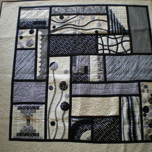 Peut inclure: Une courtepointe noire et blanche avec un motif géométrique. La courtepointe est composée de carrés et de rectangles de différentes tailles et couleurs. La courtepointe est matelassée avec un point simple.