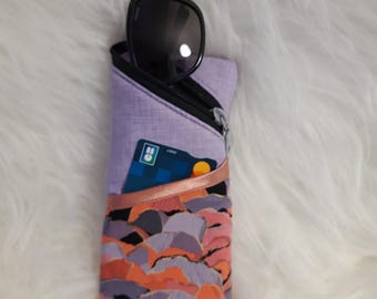 May include: A purple zippered pouch with a black zipper and a colorful abstract print. A pair of sunglasses and a credit card are inside the pouch.