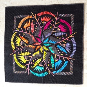 Peut inclure: Une courtepointe colorée avec un motif circulaire présentant une variété de formes et de motifs géométriques. La courtepointe est faite de tissu dans des tons de rouge, orange, jaune, vert, bleu, violet et noir. La courtepointe est matelassée avec un fil noir.