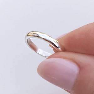May include: A polished silver band ring with a smooth, rounded exterior surface and a reflective metallic finish. The ring features a simple, continuous circular design with a consistent width throughout the entire circumference of the metal band.