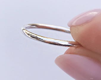 Op de afbeelding: Een dunne, gepolijste zilverkleurige metalen ring met een gladde, ronde band. De ring heeft een eenvoudig, doorlopend cirkelvormig ontwerp met een reflecterend, metalen oppervlak dat het licht opvangt en een strakke uitstraling geeft.