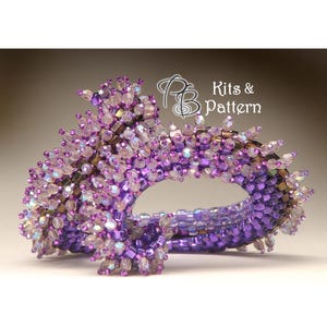 May include: A beaded bracelet in shades of purple and iridescent colours. The bracelet is made with various bead shapes and sizes, creating a textured effect. The text "Kits & Pattern" is visible. A unique, handcrafted accessory.