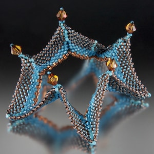 Könnte beinhalten: Ein sternförmiges Schmuckstück aus blauen und kupfernen Perlen mit Kristall-Akzenten.