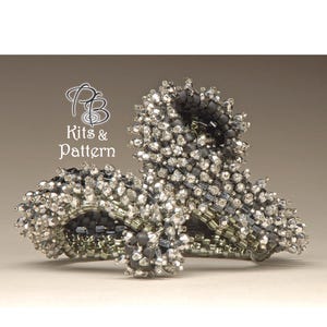 Puede incluir: Una pieza de joyería de cuentas plateadas y negras con un diseño abstracto único. La pieza está hecha de cuentas pequeñas y redondas y tiene un aspecto texturizado y orgánico.