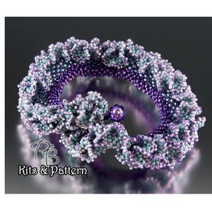 Puede incluir: Un brazalete de cuentas de color morado y azul con un diseño floral. El brazalete está hecho con cuentas pequeñas e iridiscentes y tiene un aspecto delicado y femenino.