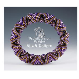 Puede incluir: Un brazalete de cuentas de color morado, dorado y negro con un diseño en espiral. El brazalete está hecho con pequeñas cuentas de semillas y es una pieza llamativa. Paulette Baron Designs Kits & Pattern.