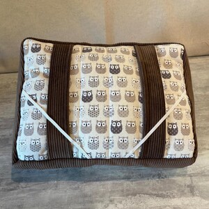 Peut inclure: Coussin rectangulaire avec une bordure en velours côtelé marron et deux bandes verticales en velours côtelé. Le tissu central présente un motif répété de hiboux dans les tons de gris et de marron. Un élastique blanc traverse le coussin.