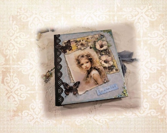 Peut inclure: Un journal fait à la main avec une couverture bleu clair représentant un portrait de jeune fille, des papillons et des motifs floraux. Le journal a une bordure en dentelle noire et une fermeture à ruban bleu. Le texte sur le journal dit "You are so loved!"
