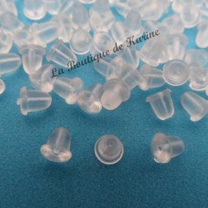 Peut inclure: Gros plan sur un tas de dos d'oreille en plastique transparent. Les dos sont petits et ronds, avec un petit trou au centre. Ils sont conçus pour être utilisés avec des boucles d'oreilles à clous.