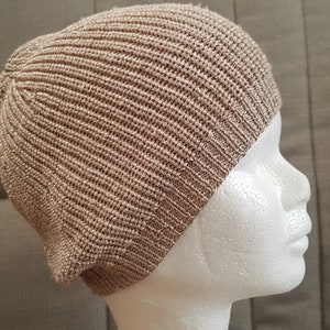May include: A light tan beanie with a vertical ribbed knit texture. The hat features a rounded crown and a fitted band at the base, constructed from a consistent yarn material that covers the top and sides of the head in a simple, solid design.