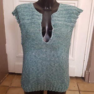Puede incluir: Top sin mangas de punto color turquesa con cuello en V pronunciado. El top, exhibido en un maniquí negro, presenta un diseño texturizado y acanalado. La prenda parece hecha a mano y es adecuada para climas cálidos.