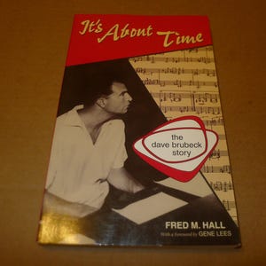May include: A book titled It's About Time: The Dave Brubeck Story by Fred M. Hall with a foreword by Gene Lees. The cover features a black and white photograph of Dave Brubeck at a piano, overlaid with musical notation and a red graphic.