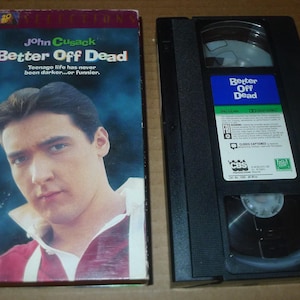 May include: A VHS tape and its case for the movie "Better Off Dead" starring John Cusack. The case features a portrait of the actor and the movie title. The VHS tape is black with a blue and green label.