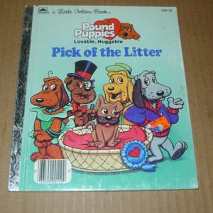 May include: A vintage "Little Golden Book" titled "Pound Puppies: Pick of the Litter." The cover features cartoon illustrations of several dogs, including a brown puppy in a basket, and the text "Lovable, Huggable."