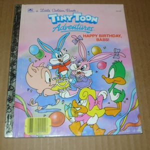 May include: A Little Golden Book titled "Tiny Toon Adventures" with cartoon characters celebrating a birthday. The cover features a pig, two rabbits, a duck, and a yellow duck. The text "Happy Birthday, Babs!" is also visible.