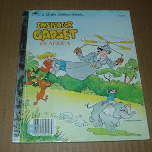 May include: A Little Golden Book titled "Inspector Gadget in Africa." The cover features Inspector Gadget flying with a helicopter hat, a girl, a dog, and a boy riding an elephant. The background is a green landscape.