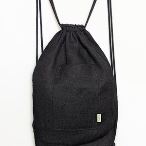 Pode incluir: Mochila preta de lona com cordão de ajuste e um pequeno bolso na frente. A mochila tem uma etiqueta que diz "hemptique".