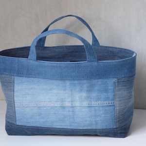 Op de afbeelding: Een grote blauwe denim tote bag met een patchwork ontwerp. De tas heeft twee handvatten en is gemaakt van gerecycled denim.